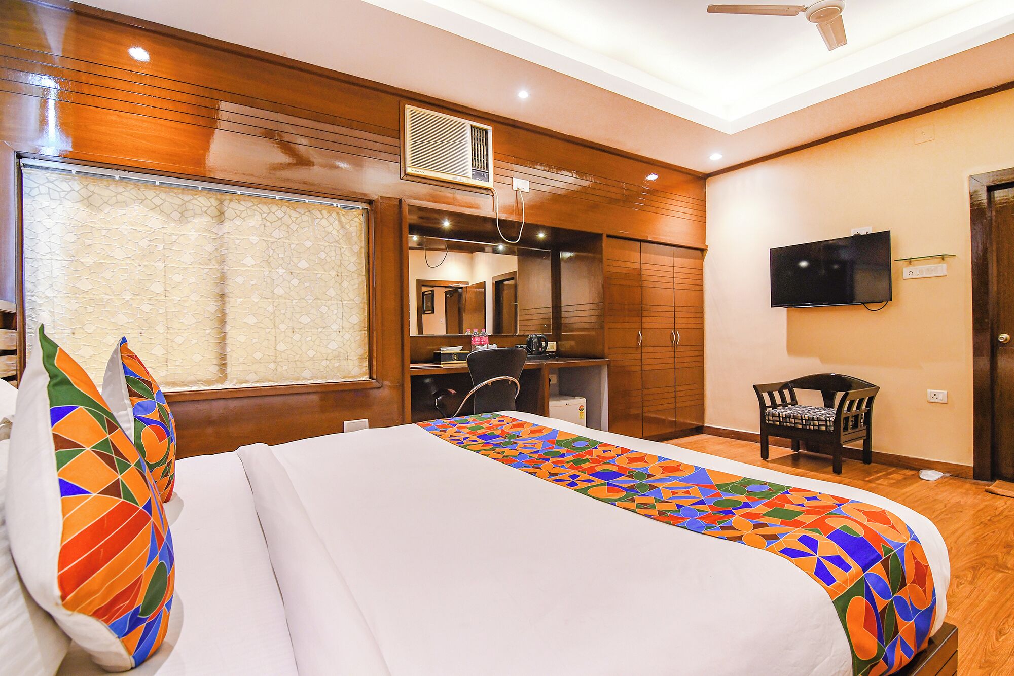 Quarto de hotel com uma cama, escrivaninha, cadeira, televisão e guarda-roupa.