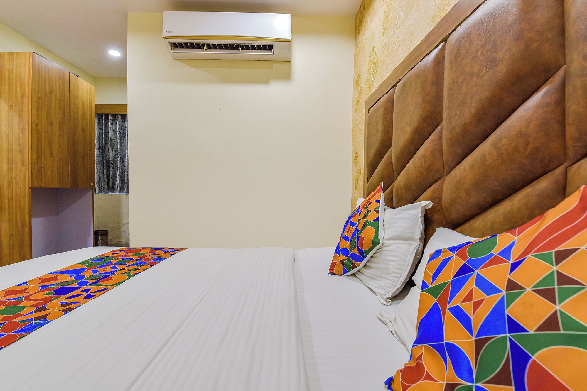 Een hotelkamer met een bed, een kussen, een kleurrijke deken, een hoofdbord en een airconditioning.