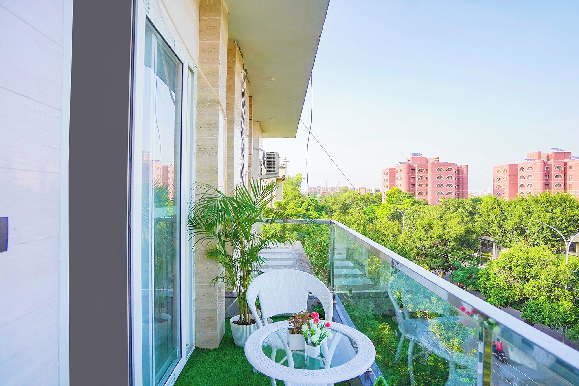 Un balcone con un tavolo e sedie in vetro, una pianta in vaso e vista sugli edifici circostanti.