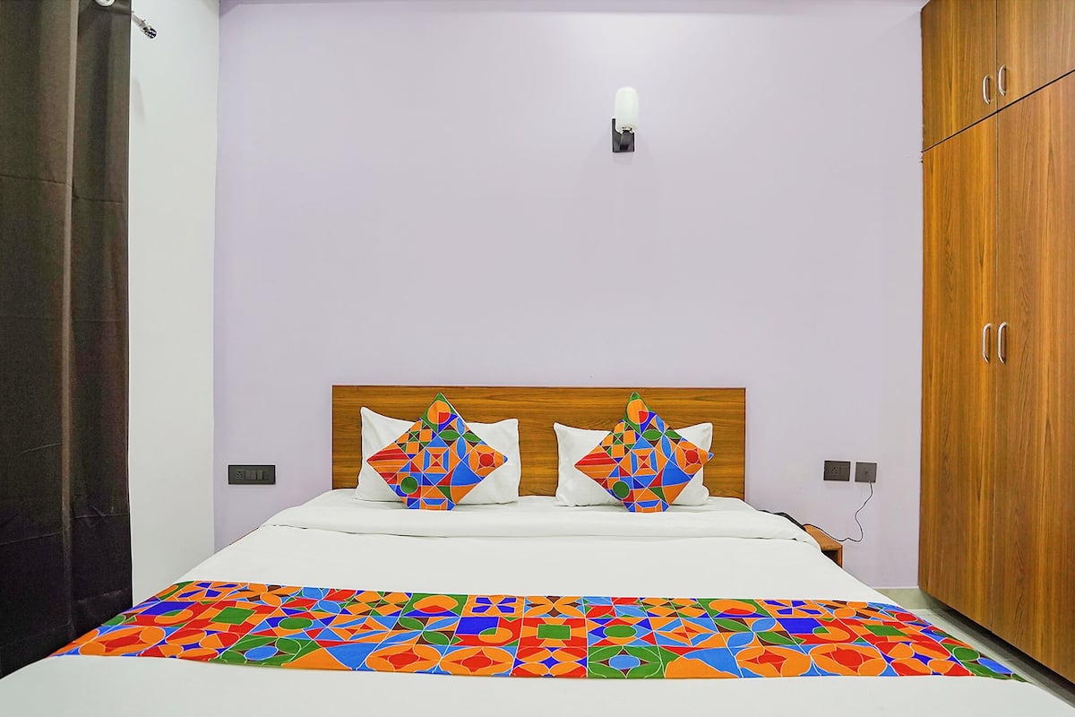 A bedroom with a bed, two pillows, a wooden wardrobe, and a wall-mounted light.