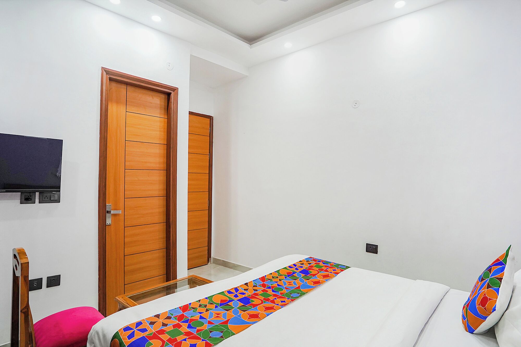 A bedroom with a bed, a TV mounted on the wall, and wooden doors.