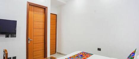 A bedroom with a bed, a TV mounted on the wall, and wooden doors.