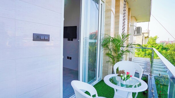 Un balcón con puerta de vidrio, muebles de mimbre blanco y una pequeña mesa con flores.