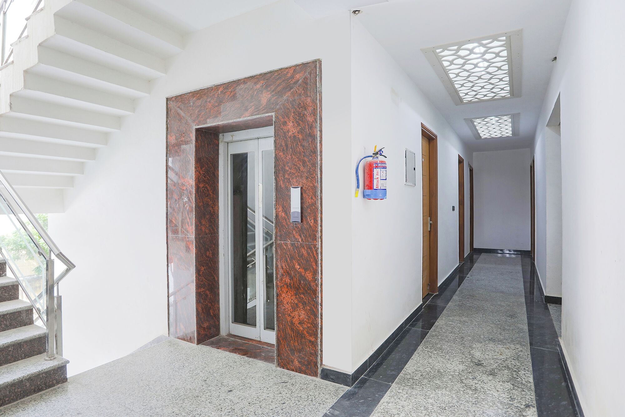 A hallway with a marble door, a fire extinguisher, and a staircase.