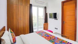 Un dormitorio con cama, armario de madera, televisor y ventana con cortinas.