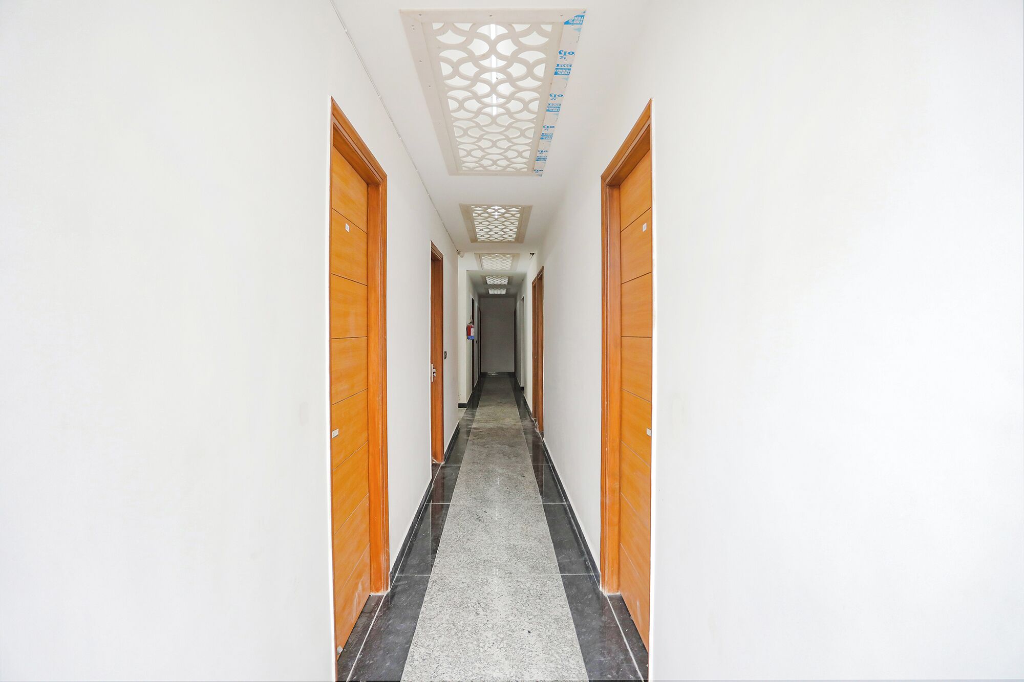 A hallway with wooden doors, a patterned ceiling, and a tiled floor.