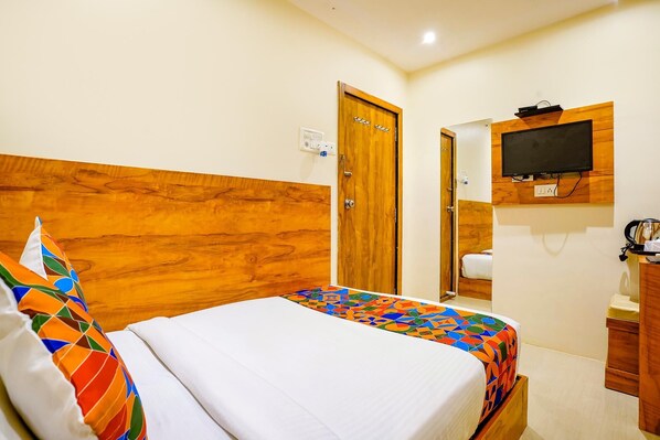 A hotel room with a wooden headboard, a bed with a colorful bedspread, a television mounted on the wall, and a wooden cabinet.