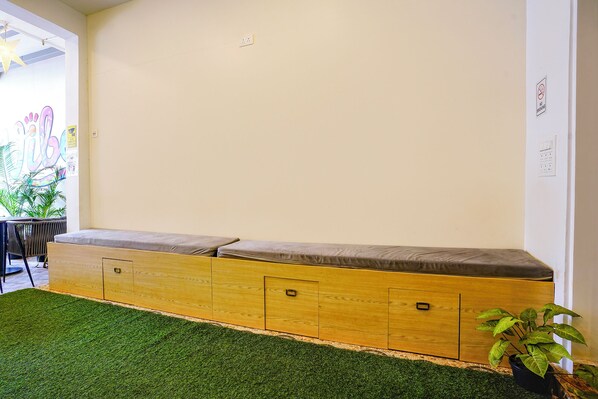 A room with a wooden bench against a wall, a green artificial grass floor, and a potted plant. - Fabhotel Vibes (Vagator)