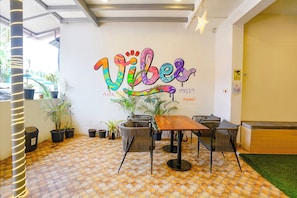 A room with a tiled floor, a wooden table, and chairs. There is a wall with a colorful mural and some potted plants. - Fabhotel Vibes (Vagator)