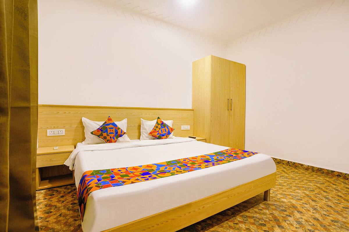 A neatly made bed with a colorful geometric-patterned bedspread, a wooden headboard, and a matching wooden wardrobe.