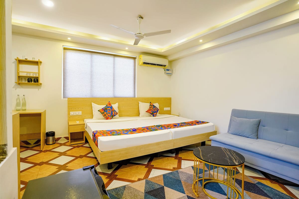 A hotel room with a bed, a blue sofa, a small table, and a ceiling fan.