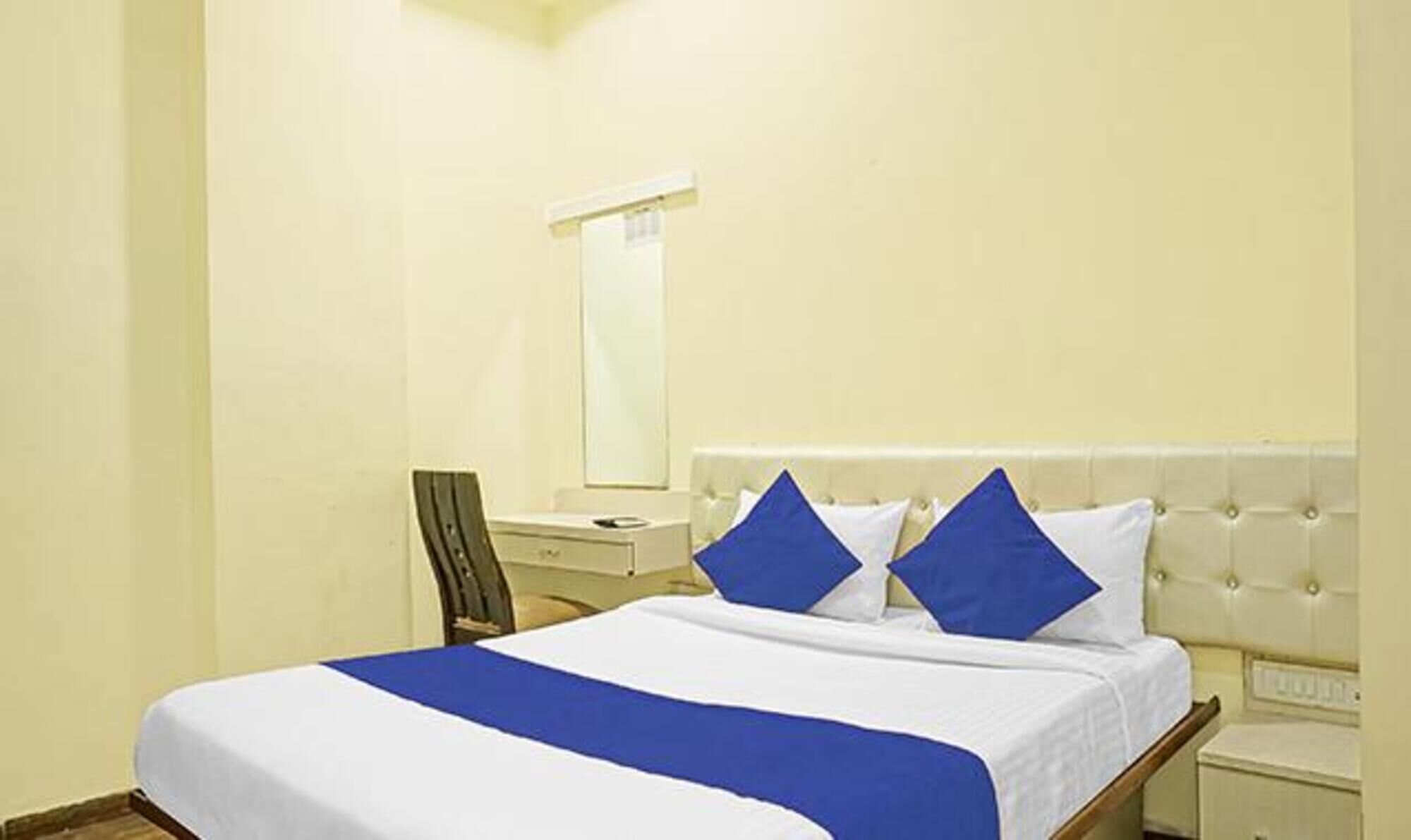 A hotel room with a bed, a nightstand, a chair, and a mirror on the wall.