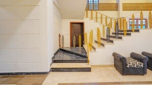 Una escalera con barandillas doradas ornamentadas, una puerta de madera oscura y un sofá con un cojín estampado.