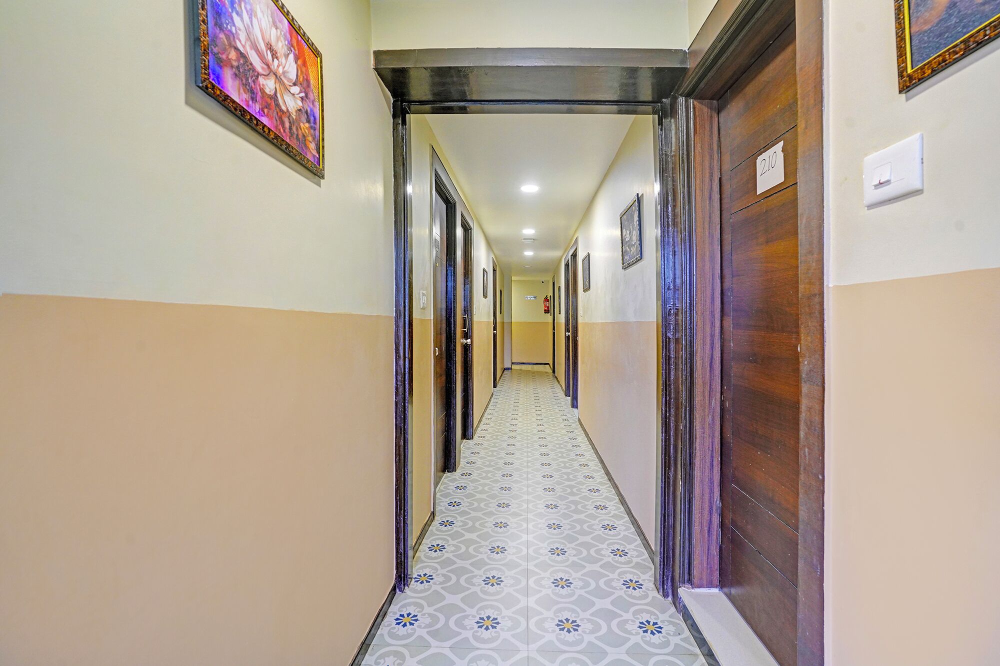 A hallway with patterned floor tiles, wooden doors, and a framed picture on the wall.