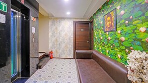 A hotel lobby with a patterned floor, a wooden bench, a door with the number 202, and a wall mural of lotus flowers.