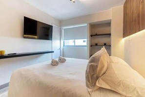 Ein modernes Hotelzimmer mit einem großen Bett, einem flachbildfernseher an der Wand und Blick auf die Stadt durch ein großes Fenster.