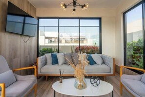 A modern living room with a sofa, two armchairs, a coffee table, and a TV mounted on the wall.