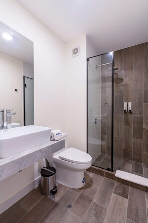 A modern bathroom with a glass shower enclosure, a marble countertop, and a toilet.