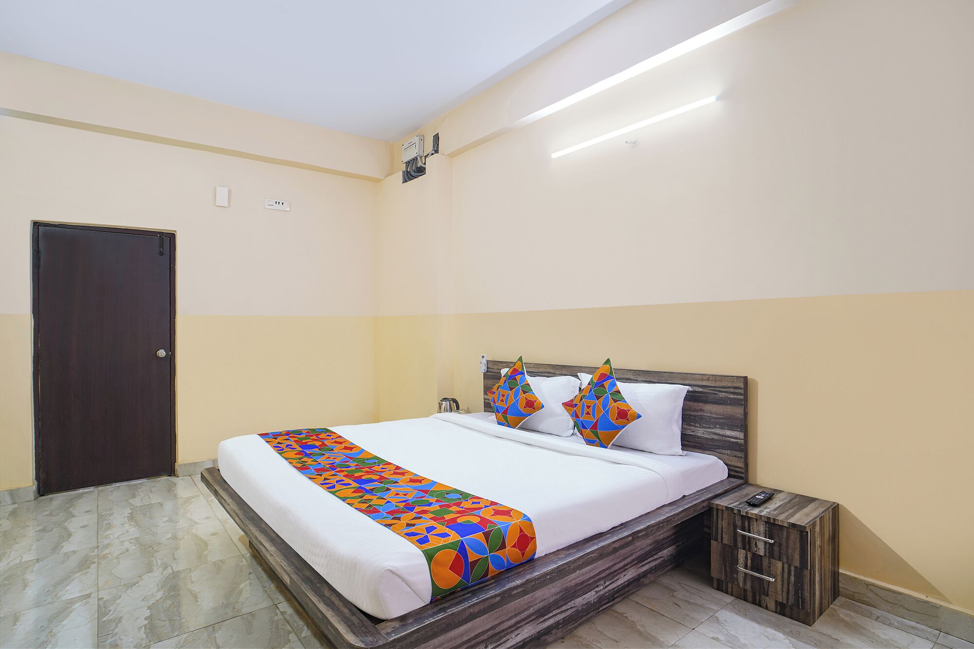 A hotel room with a bed, a nightstand, a wooden headboard, a door, and a light fixture.