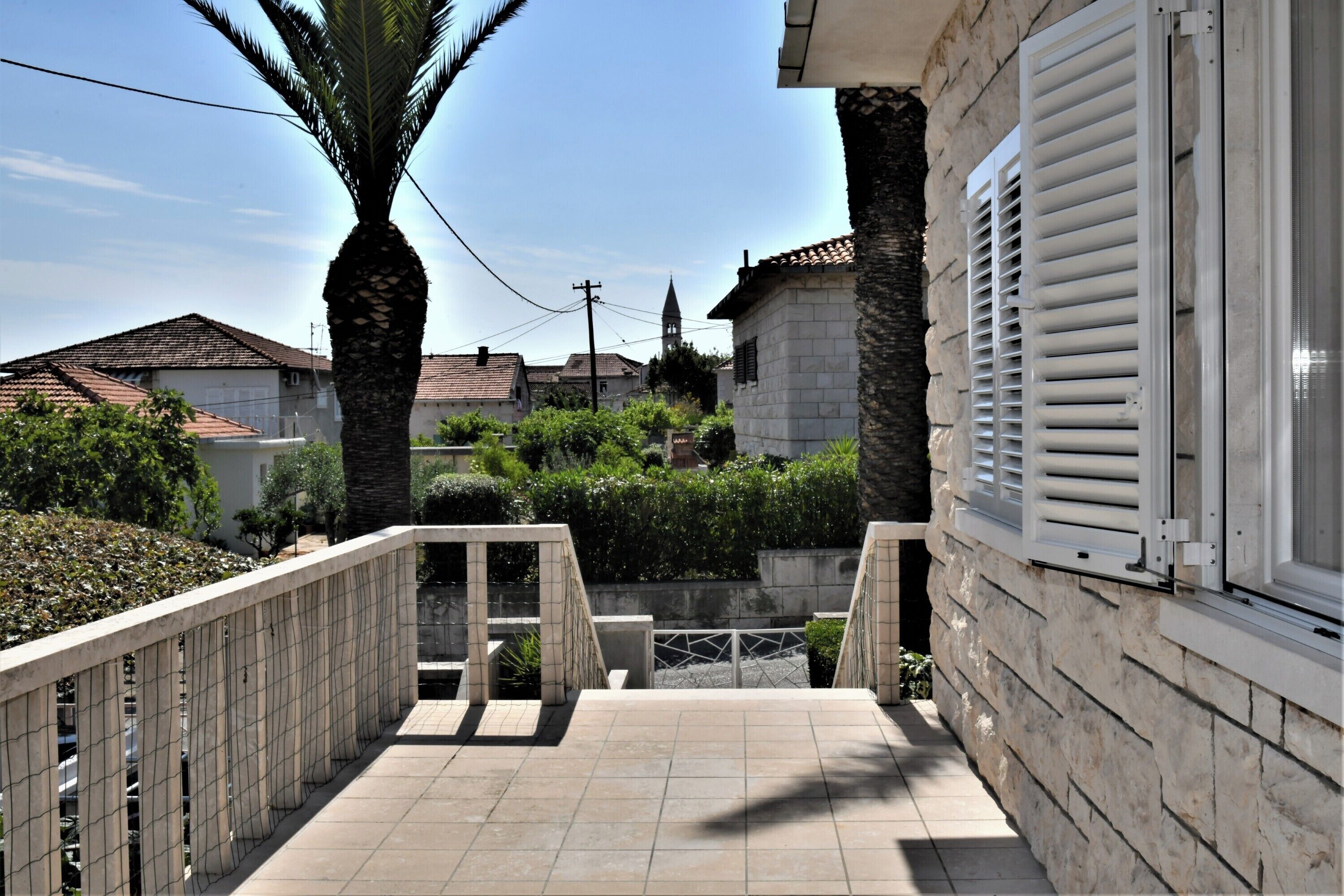 A residential building with a stone facade, a tiled balcony, and a palm tree.