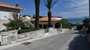 A residential street with stone walls, palm trees, and houses with red-tiled roofs.