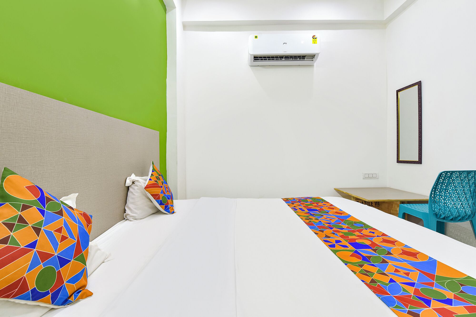 A hotel room with a bed, a desk, a chair, and an air conditioning unit.