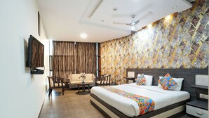 Una habitación de hotel moderna con una cama grande, un sofá, dos sillones, una mesita y un televisor montado en la pared.