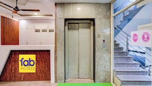 Een lift in een hotel lobby met een groen tapijt, een houten muur met een 'Fab Hotels' bord en een glazen muur met een 'STOP' bord.