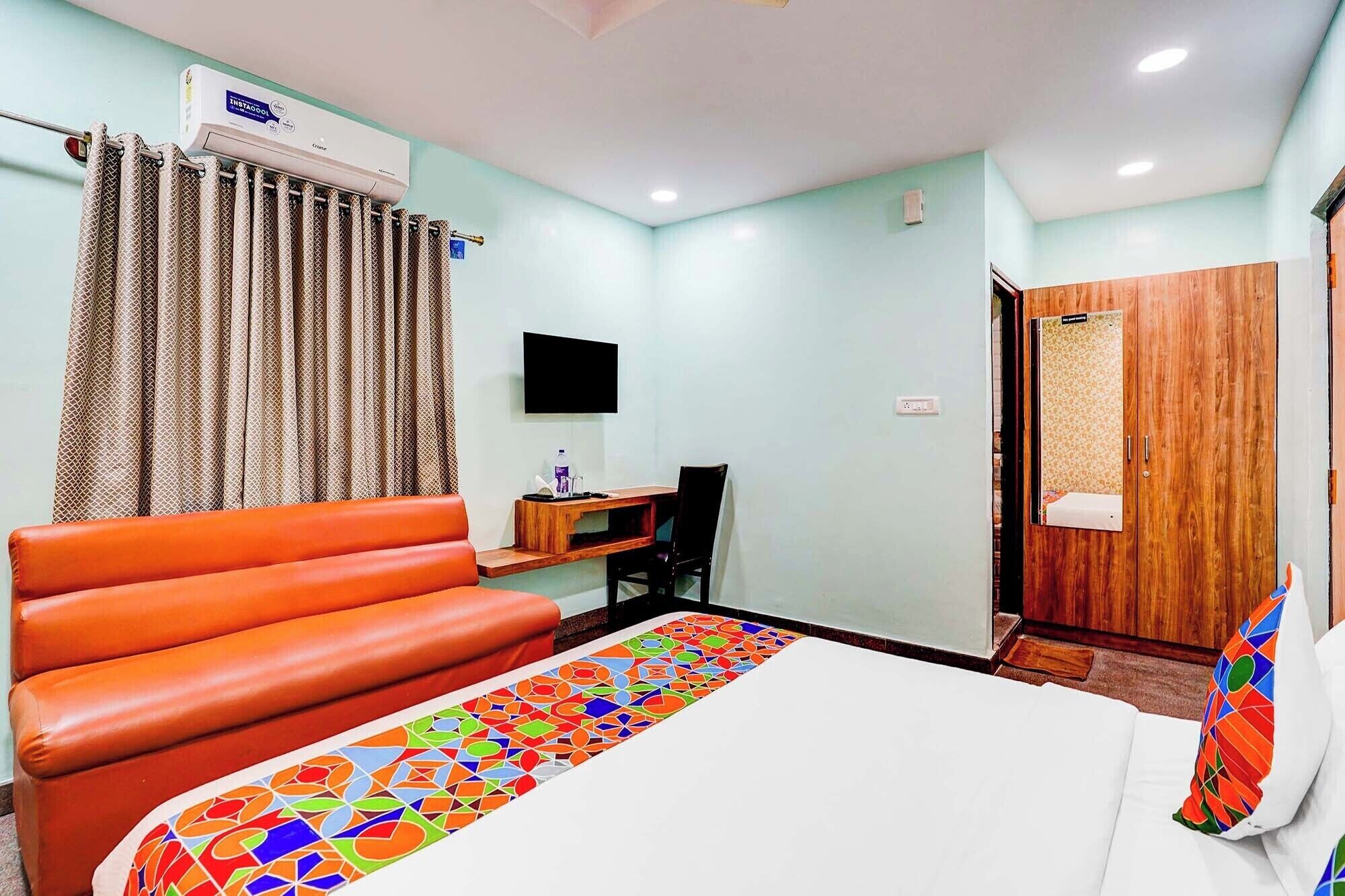 A hotel room with a bed, a sofa, a desk with a chair, a television, and a wardrobe.