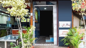 Een restaurantentree met een donker interieur, potplanten en een trap die naar binnen leidt.