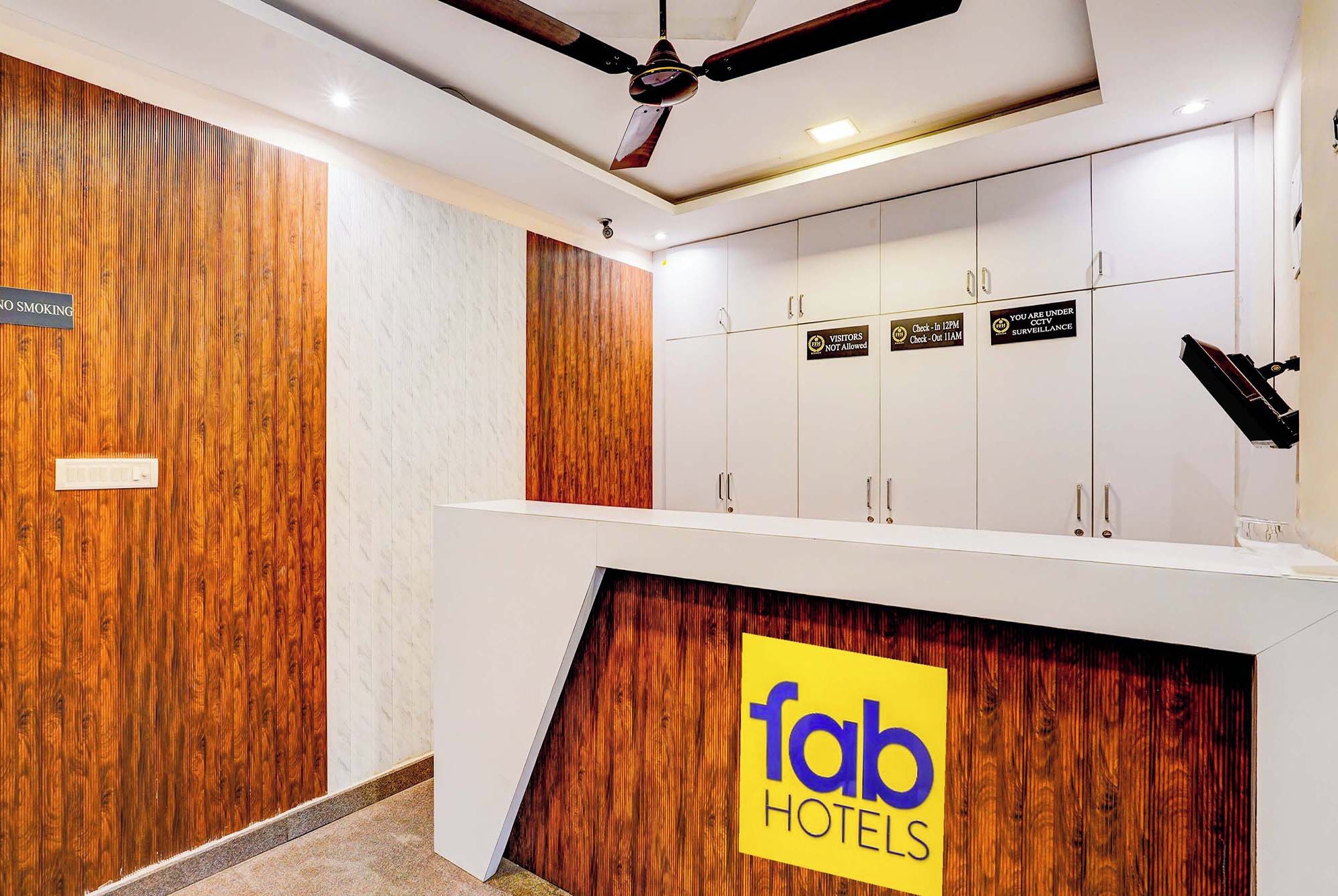 A hotel reception area with a wooden accent wall, a ceiling fan, and a sign indicating 'fab hotels'.