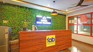 A hotel reception desk with a wooden counter, a digital screen displaying the hotel name, and a green wall with plants. - Fabhotel Blue Diamond (Hyderabad)