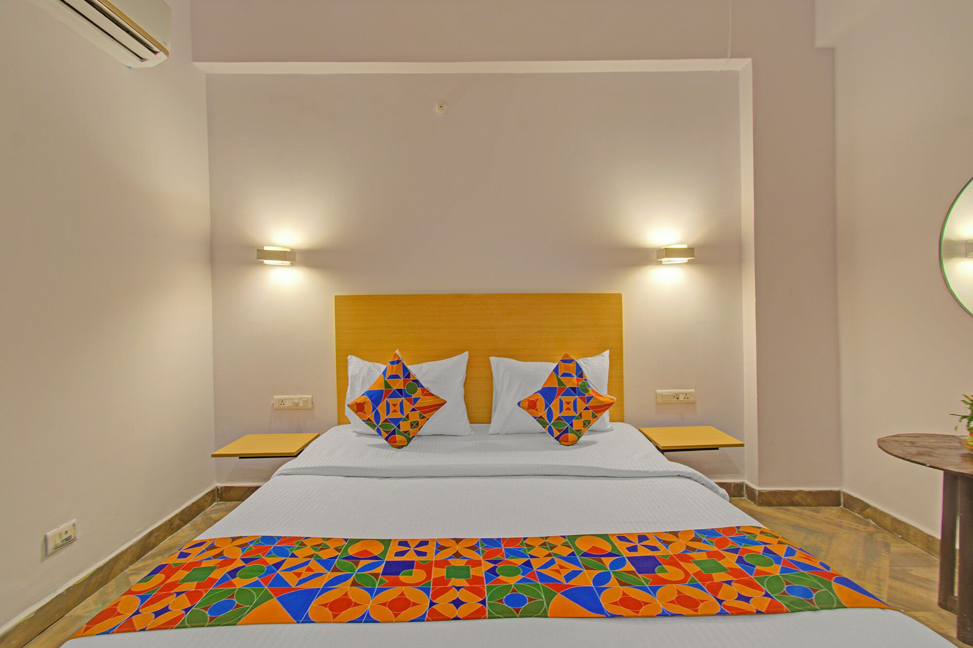 Une chambre d’hôtel avec un lit, deux oreillers, des tables de chevet, une commode, un miroir et une couvre-lit à motifs.