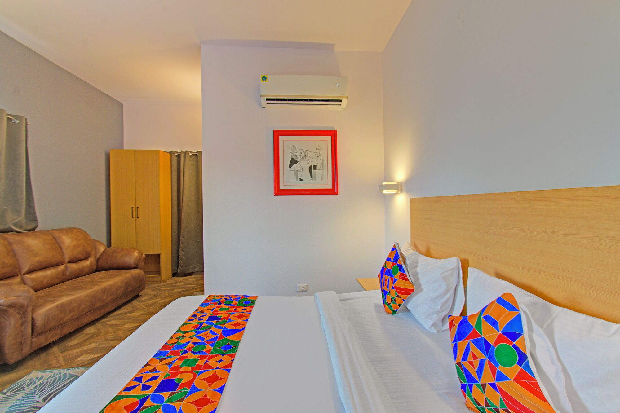 A hotel room with a bed, a sofa, an air conditioner, and a framed picture on the wall.