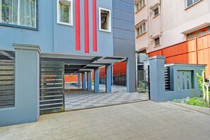 Ein überdachter Parkbereich mit befestigter Einfahrt, Schachbrettmuster-Boden und einem Gebäude mit vertikalen roten Streifen und Fenstern.