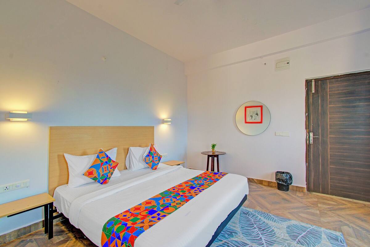 A hotel room with a bed, bedside tables, a small round table with a plant, a mirror on the wall, and a door.