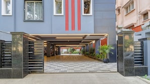 Uma entrada de prédio moderna com uma galeria coberta, piso xadrez e plantas em vasos.
