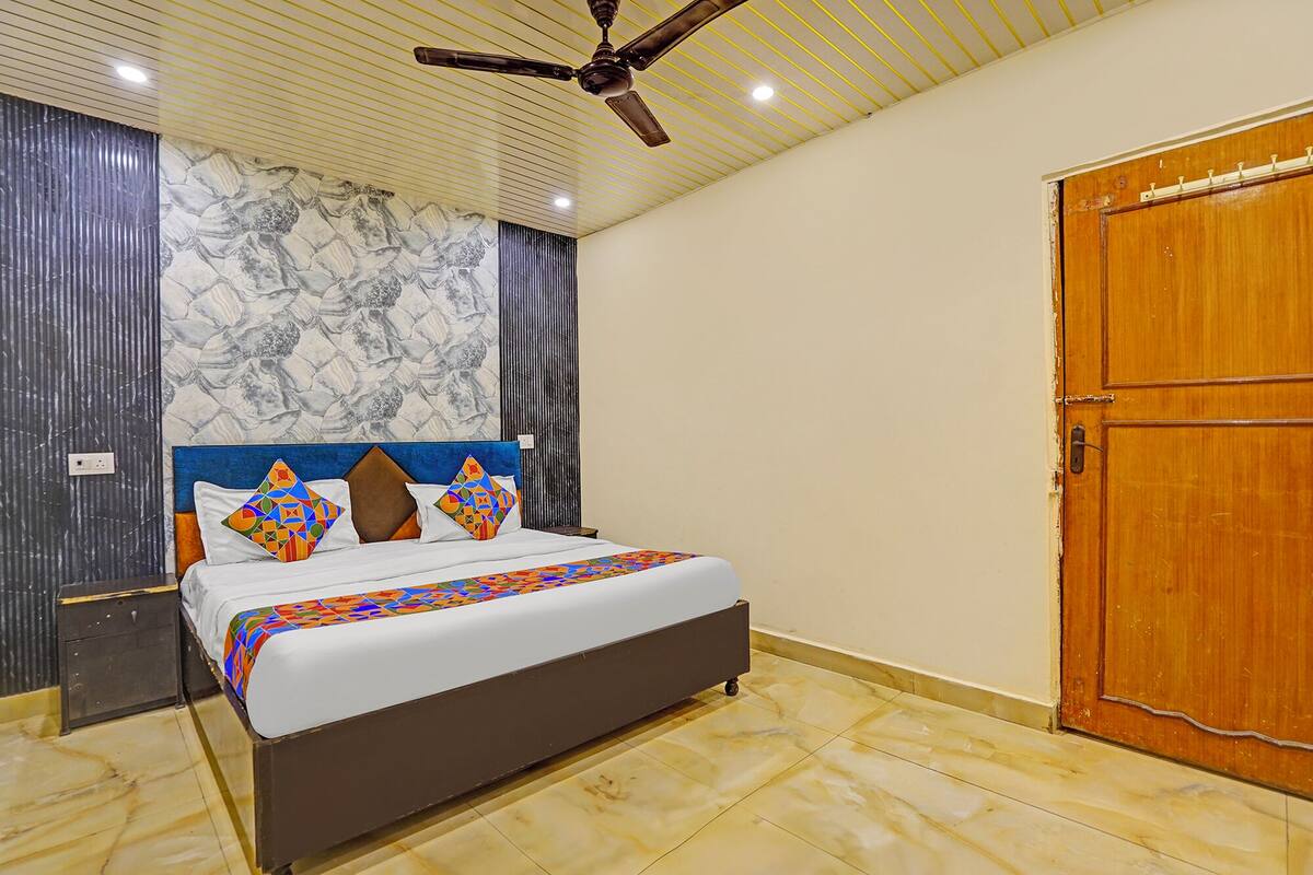 Une chambre à coucher avec un lit, un ventilateur de plafond, un mur décoré d’un motif imitant le marbre et une porte en bois.