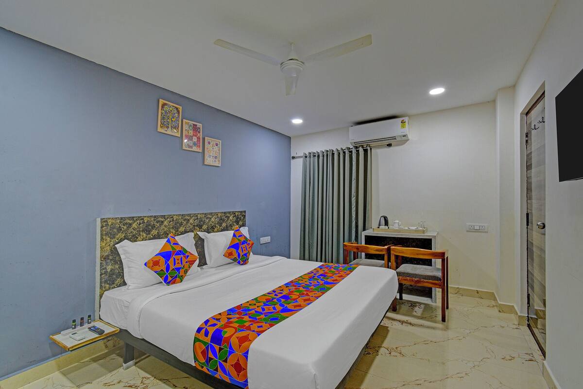 A hotel room with a bed, a desk, a chair, a ceiling fan, and an air conditioning unit.