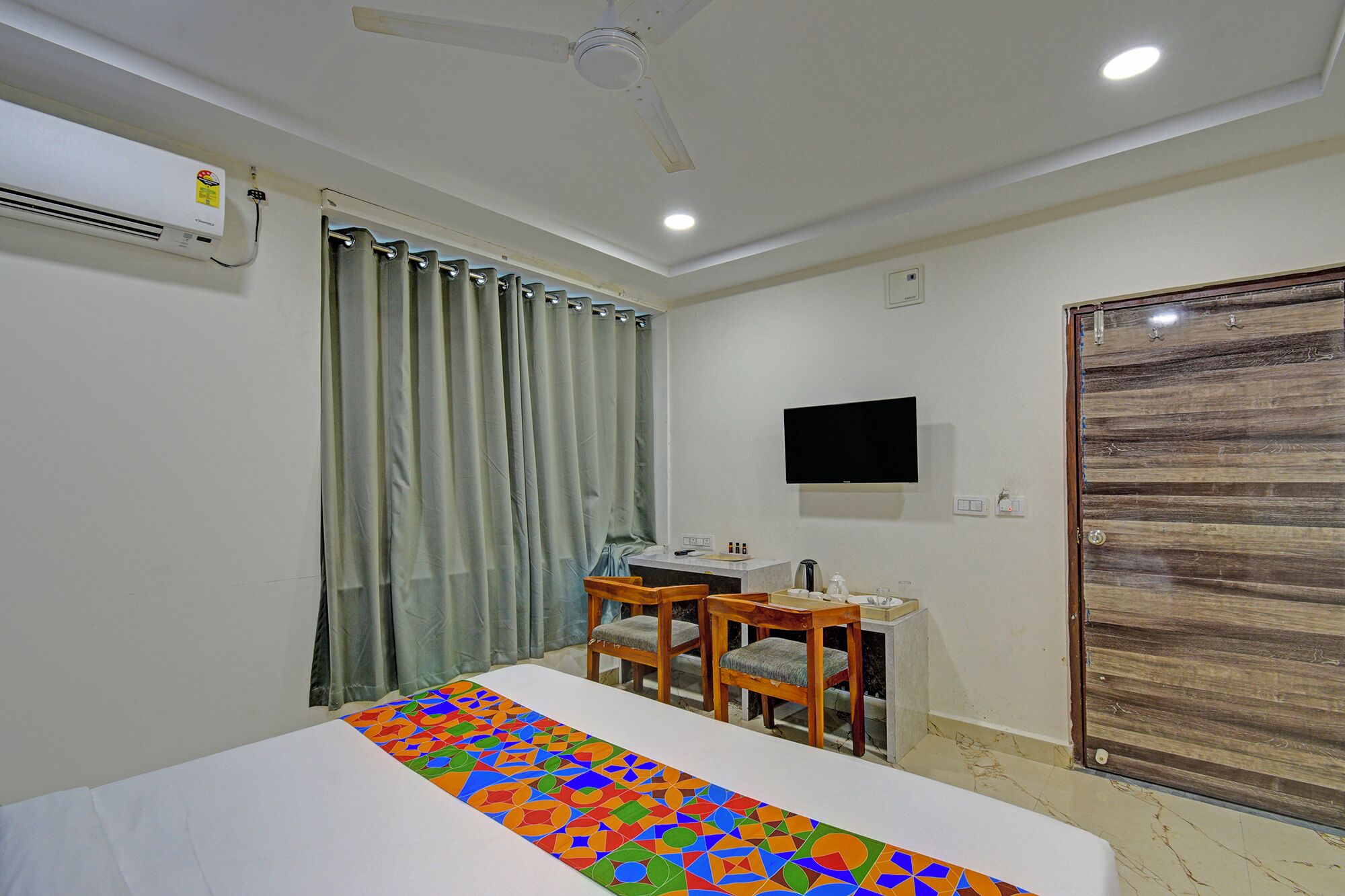 A hotel room with a bed, a desk with chairs, a television, and a window with curtains.