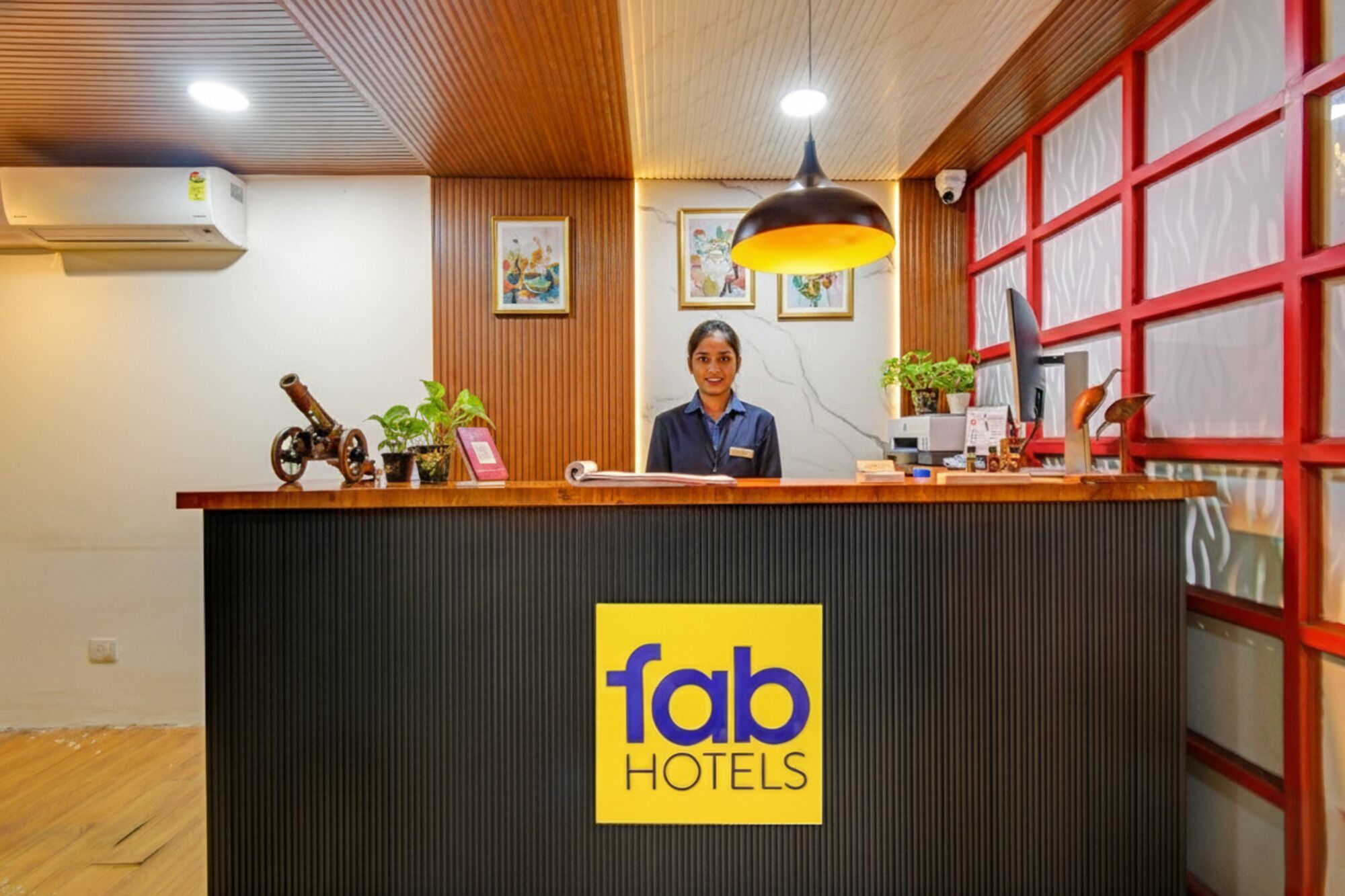 Et hotelreceptionsområde med en logo, en receptionist samt diverse genstande såsom en lampe, planter og et vintage kamera.