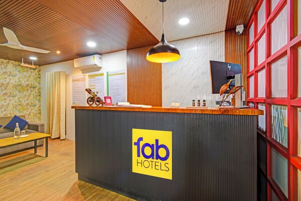 A reception desk with a sign reading "fab hotels" in a hotel lobby with wooden paneling, a ceiling fan, and a red-framed window.
