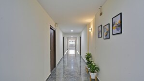 A long, narrow hallway with marble flooring, white walls, and a few potted plants. - Fabhotel Rio (Hyderabad)
