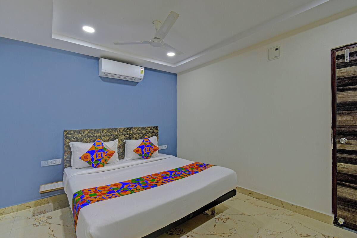 A bedroom with a bed, blue walls, a ceiling fan, an air conditioner, and a wooden door.