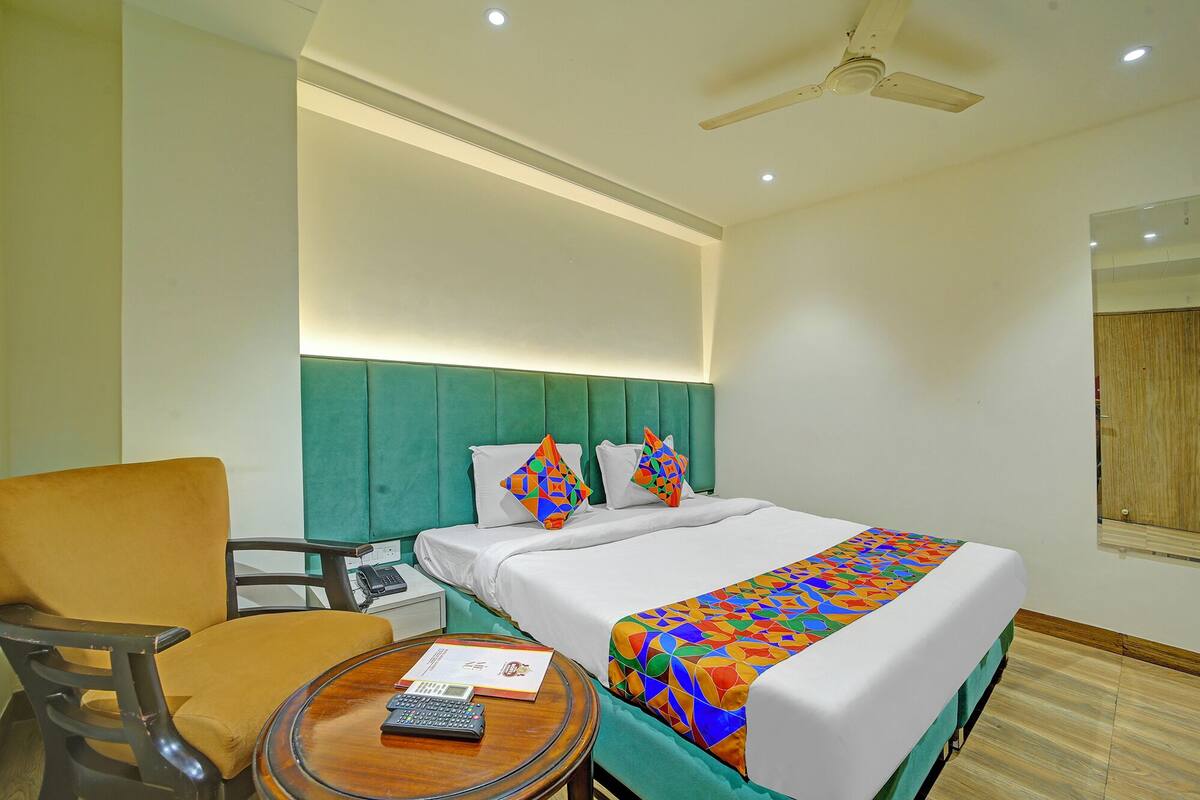 A hotel room with a bed, a chair, a small table with a remote control, and a ceiling fan.