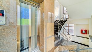 Un intérieur moderne avec un ascenseur en verre, un escalier et un système d’alarme incendie.