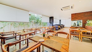 Un restaurant spacieux, doté de meubles en bois et d’une grande fenêtre donnant sur un espace verdoyant.