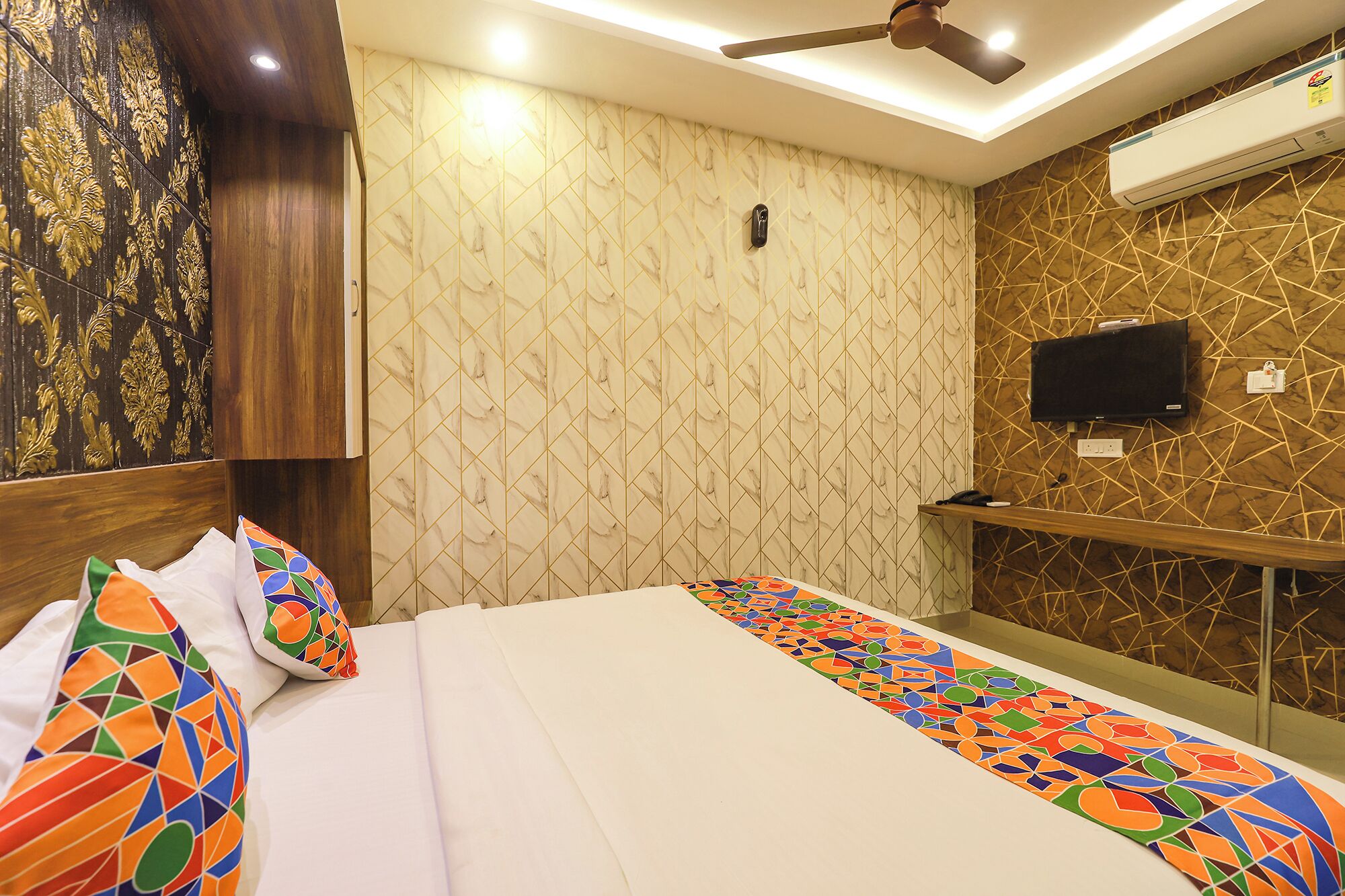 Une chambre d’hôtel avec un lit, un téléviseur fixé au mur et un ventilateur de plafond.