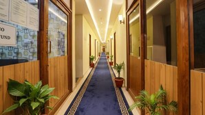 A hotel corridor with wooden paneling, a blue carpet, and potted plants. - FabHotel Joy Residency (Chennai)