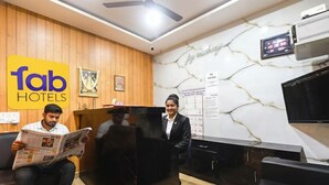 A hotel reception area with wooden paneling, a marble wall, a reception desk, and a television. - FabHotel Joy Residency (Chennai)